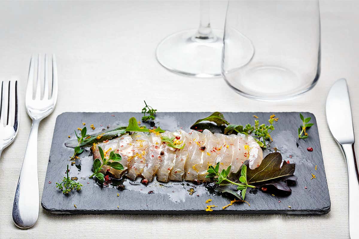 Carpaccio di orata marinata agli agrumi e erbette, olio di arancio e mandorle Carpaccio di orata marinata agli agrumi e erbette, olio di arancio e mandorle